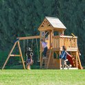 Houten speeltoestel met schommels, trapeze, klimmuur en glijbaan. Kinderen spelen buiten.
