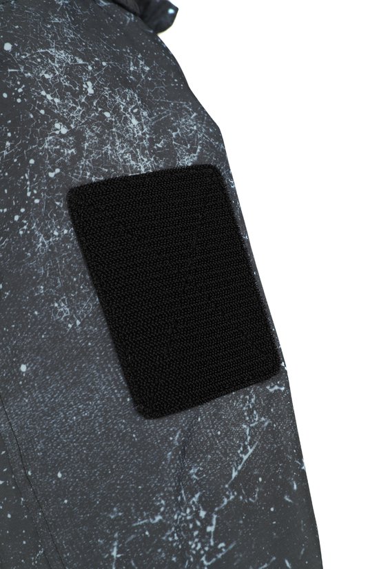 Detail van een zwarte klittenband patch op een grijze jas met een kras- en spatterprint.