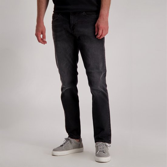 Man in een donkergrijze jeans met rechte pijpen, gedragen met grijze sneakers.