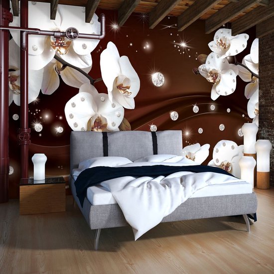 Un lit avec une tête de lit grise et des draps blancs se trouve dans une pièce avec des orchidées blanches, des diamants, des étoiles et un mur de briques.