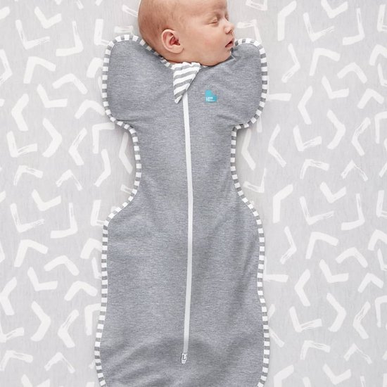 Baby slaapt in grijze Swaddle UP slaapzak met streepjesrand op grijze achtergrond met streepjespatroon.