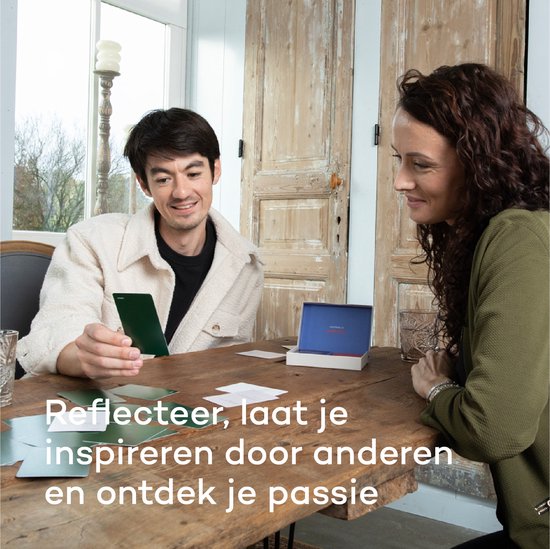 Een man en een vrouw zitten aan een tafel. De man houdt een kaart vast en kijkt ernaar. Naast hen staat een open doos met kaarten.
