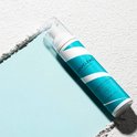 Fles met teal- en witte spiraalvormige strepen voor droogshampoo, liggend op een lichtblauwe en grijze ondergrond.