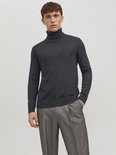 Man in donkergrijs coltrui en gestreepte broek, met de hand in de zak.