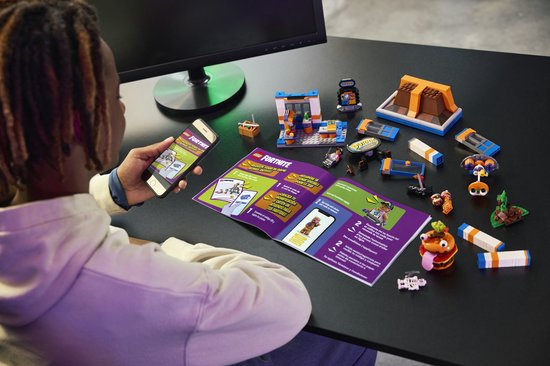Personne utilisant un téléphone près d'un livret LEGO Fortnite avec un restaurant et des pièces