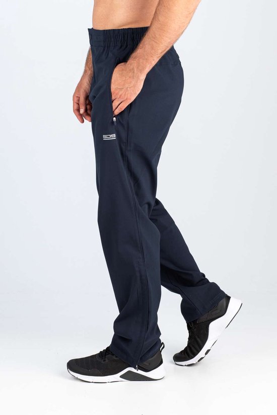 Man met donkerblauwe sportbroek met logo, elastische tailleband en zwarte schoenen.