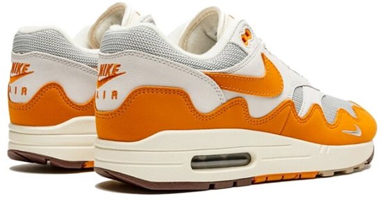 Zij-achterzicht van witte en oranje Nike Air Max 1 Patta sneakers met beige zolen en bruine details.