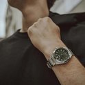 Heren horloge met zilverkleurige metalen band en donkergroene wijzerplaat. Gedragen op een mannelijke pols.