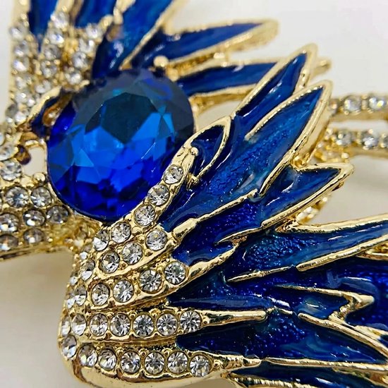 Gouden broche met een grote blauwe steen op de borst en gedetailleerde blauwe en gouden vleugels bezet met kristallen.