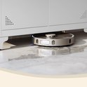Grijze robotstofzuiger die een natte vloer schoonmaakt onder een metalen kast.