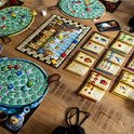 Overzicht van het bordspel De Kwakzalvers van Kakelenburg met spelborden, kaarten en fiches op een houten tafel.