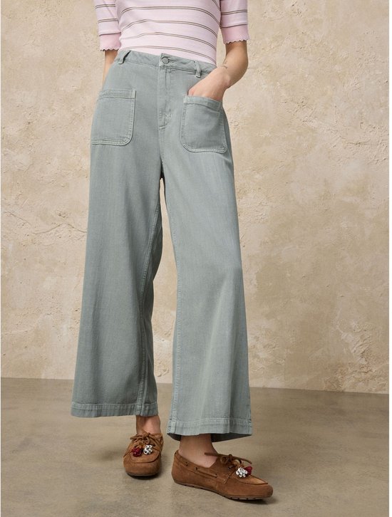 Model met lichtgroene cropped jeans met wijde pijpen en opgestikte zakken, met een gestreepte top.
