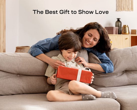 Een vrouw omhelst een jongen die een rood cadeaupakket opent. Ze zitten op een bank.