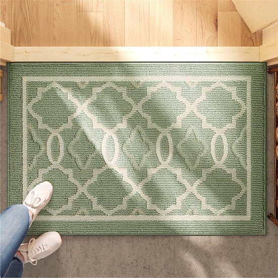 Lichtgroene deurmat met beige geometrisch patroon, met voeten in witte sneakers.
