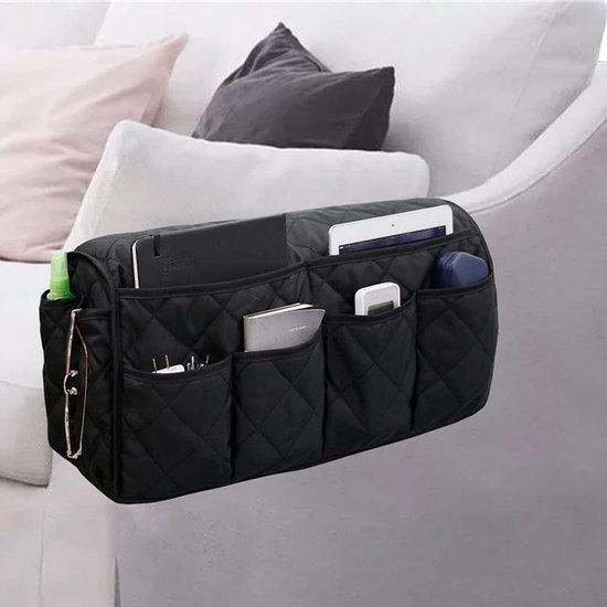 Zwarte, gewatteerde bankarmleuning organizer met meerdere vakken, vol met tablet, notitieboek, bril en flesje, op een bank.