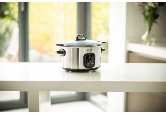 Zilverkleurige Russell Hobbs slowcooker op een aanrecht met een vaag verlichte keukenachtergrond.