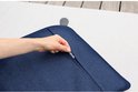 Hand die de ritssluiting opent van een donkerblauw, geweven outdoor kussen op een wit oppervlak.