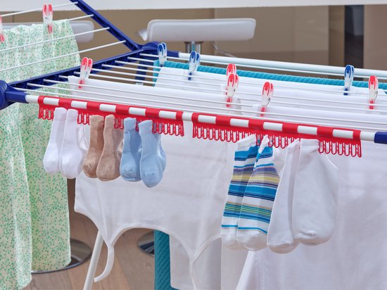 Detailopname van rode clips met sokken in diverse kleuren die aan een wit droogrek hangen.