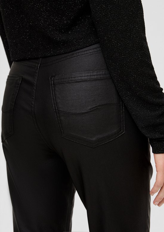 Detail van de achterzakken van een zwarte gecoate broek, gecombineerd met een zwarte glittertop.