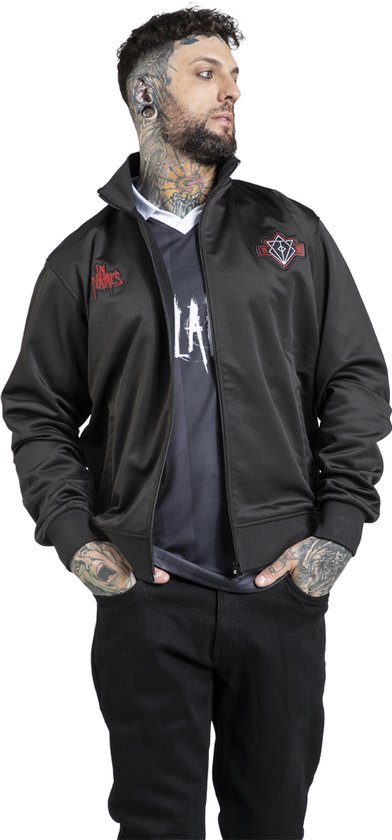 Man met tattoo's draagt zwarte trainingsjas van In Flames over een zwart-wit shirt.
