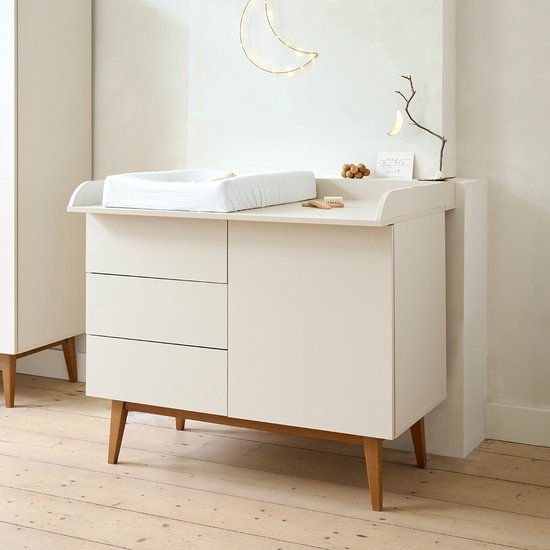 Crème commode met drie lades aan de linkerkant, een deur aan de rechterkant en houten poten.