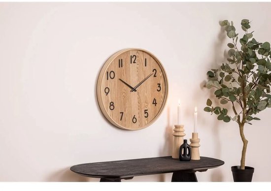 Houten wandklok met zwarte cijfers en wijzers, aan een witte muur.