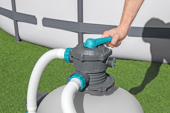Hand verstelt de hendel van de grijze zandfilterpomp bij een zwembad op gras.