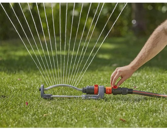 Een hand verstelt oranje hendel op een sproeier met waterstralen.