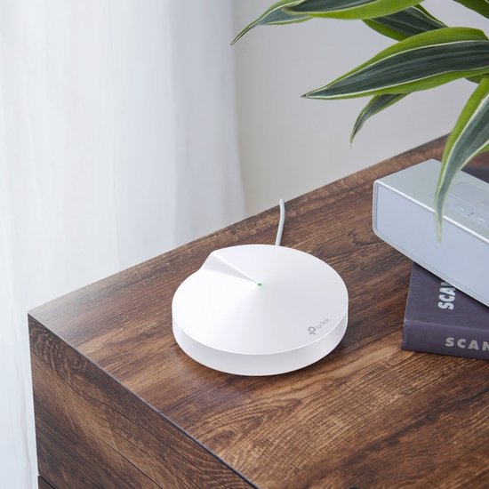 Eén wit, rond TP-Link Deco M5 mesh wifi-apparaat op een houten tafel naast een plant en een speaker.