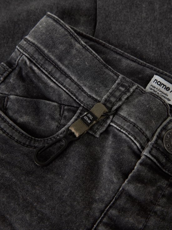Sluiting van een donkergrijze spijkerbroek met "ORG. DENIM" label.