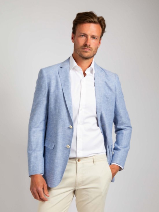 Man in lichtblauwe linnen blazer, wit overhemd en beige broek. Linkerhand in de zak.