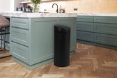 Zwarte, ronde prullenbak in een moderne keuken met lichtgroene keukenkastjes.