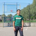 Jonge man staat op basketbalveld, draagt groene t-shirt met tekst en donkere joggingbroek.