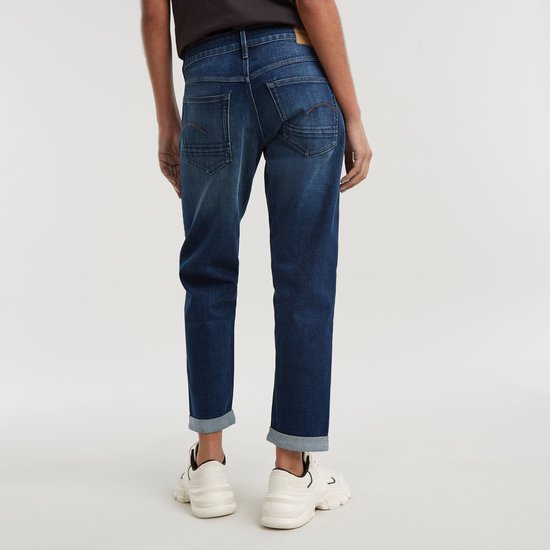 Model draagt de achterkant van een donkerblauwe jeans met omgeslagen broekspijpen.