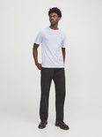 Witte T-shirt met korte mouwen en een klein zwart logo op de borst, gedragen door een man.