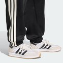 Detail van de broekspijpen van een zwarte trainingsbroek met witte strepen, gedragen met witte sneakers.