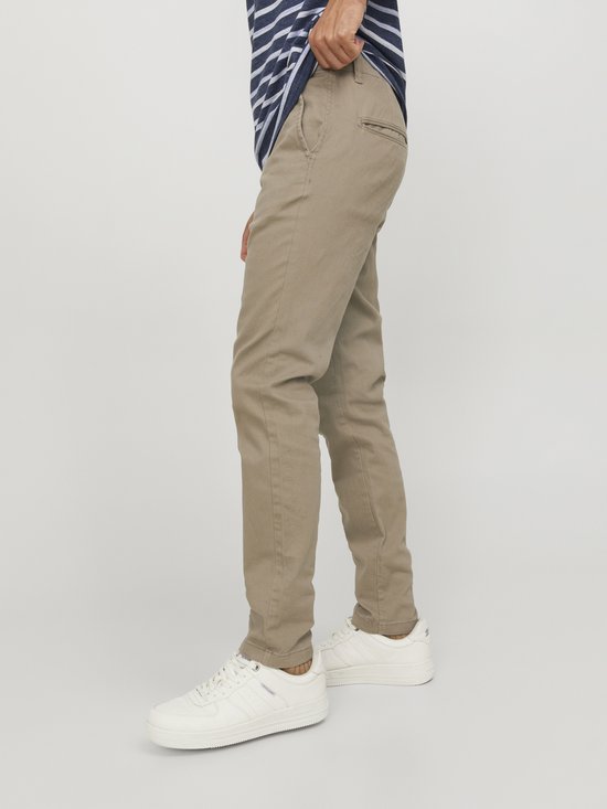 Model in een beige chino, gefocust op de broek. De achterzak met logo is zichtbaar.