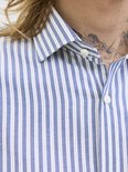 Een man met tatoeages op de nek, draagt een blauw-wit gestreept overhemd met witte knopen.