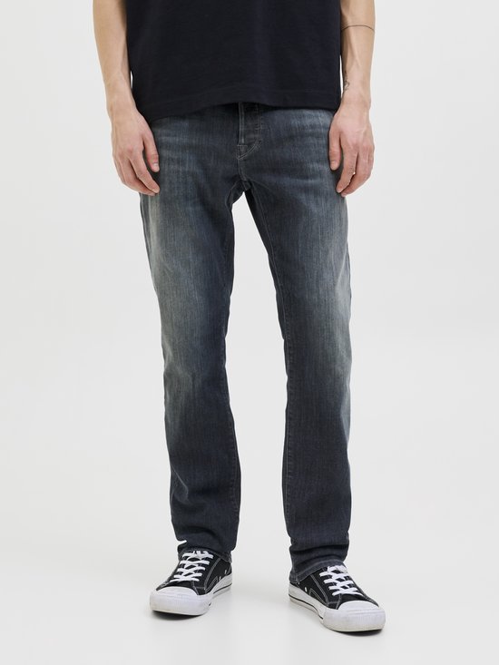 Onderlichaam van een man in donkere jeans en sneakers.