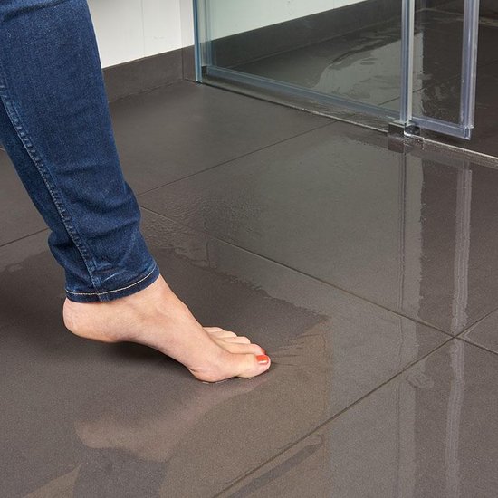 Detail van voeten van een vrouw met rode nagellak, staand op een natte, donkergrijze tegelvloer in een badkamer.