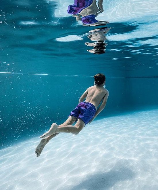 Jongetje zwemt onder water in een paarse zwembroek met een patroon.
