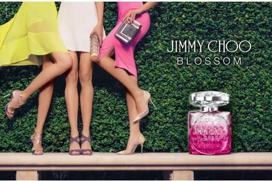 Drie vrouwenbenen met hakken bij een Jimmy Choo Blossom parfumfles en heg.