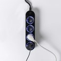 Zwarte Shelly Power Strip 4 Gen4 stekkerdoos met vier stopcontacten die blauw oplichten, met aangesloten kabels.