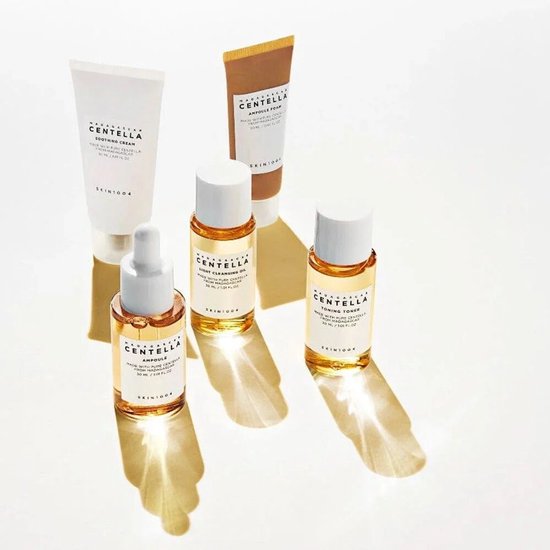 Vijf SKIN1004 Madagascar Centella-producten op een witte ondergrond, met dramatische schaduwen. Ampul, toning toner, light cleansing oil, ampoule foam en soothing cream.