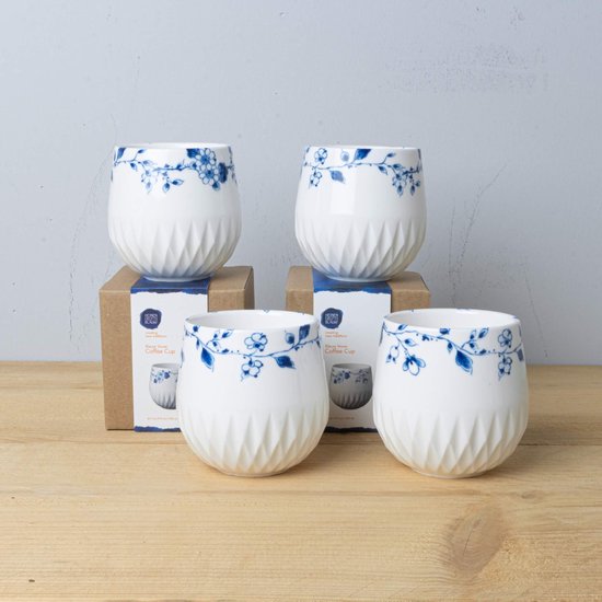 Vier witte porseleinen koffiekopjes met een blauw bloemmotief en een geribbeld onderste gedeelte op bruine verpakkingen.
