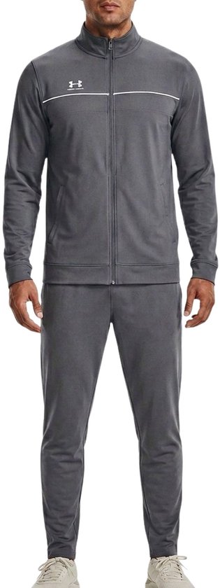 Man met donkere huid, volledig gekleed in een grijs trainingspak. Het pak heeft witte accenten.
