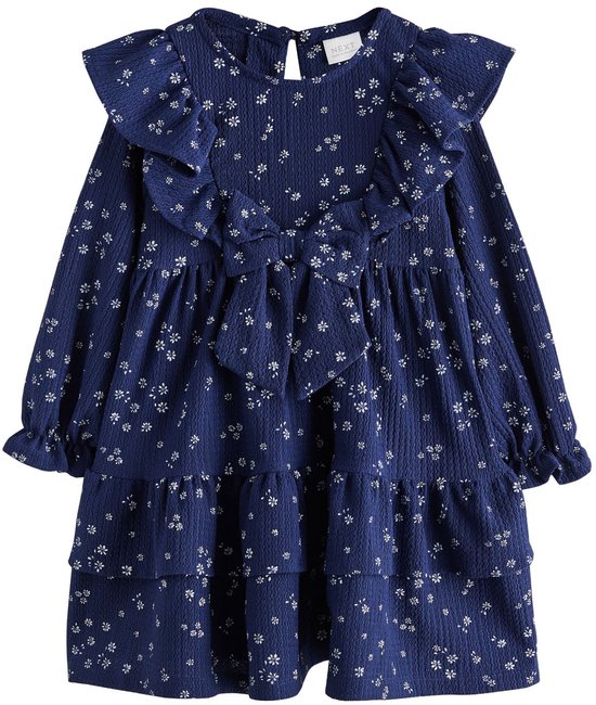 Donkerblauwe jurk met bloemenprint, ruches bij de hals, strik op de borst en gelaagde rok.