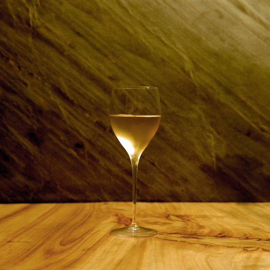 Een glas witte wijn op een houten tafel, met een schuine marmeren achtergrond.