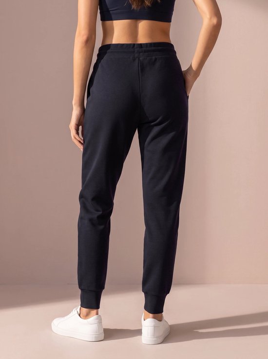 Donkerblauwe sportbroek met gedefinieerde pijpen en elastische enkelbanden, gedragen door een model met witte sneakers.
