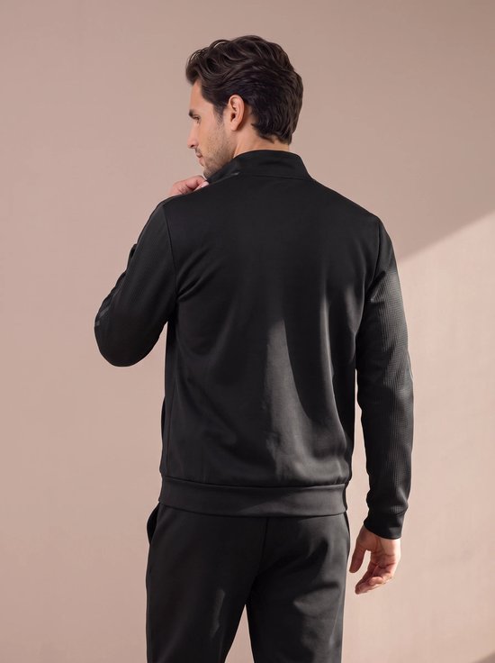 Man in zwart sportvest, achterkant met gemodelleerde mouwen en opstaande kraag.